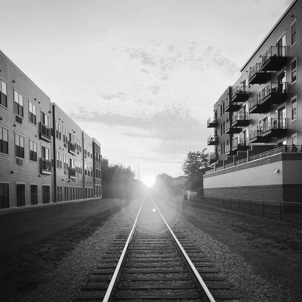 the sun reverberates at the end of a train track situated between two apartment buildings  